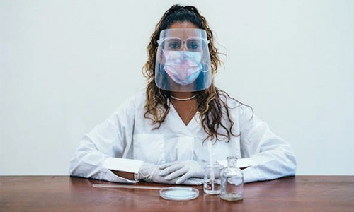 A Woman in White Lab Coat Looking while Wearing Face Mask and Face Shield