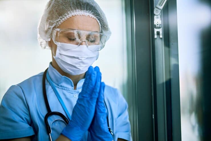 Female healthcare worker with hands clasped praying at a medical clinic